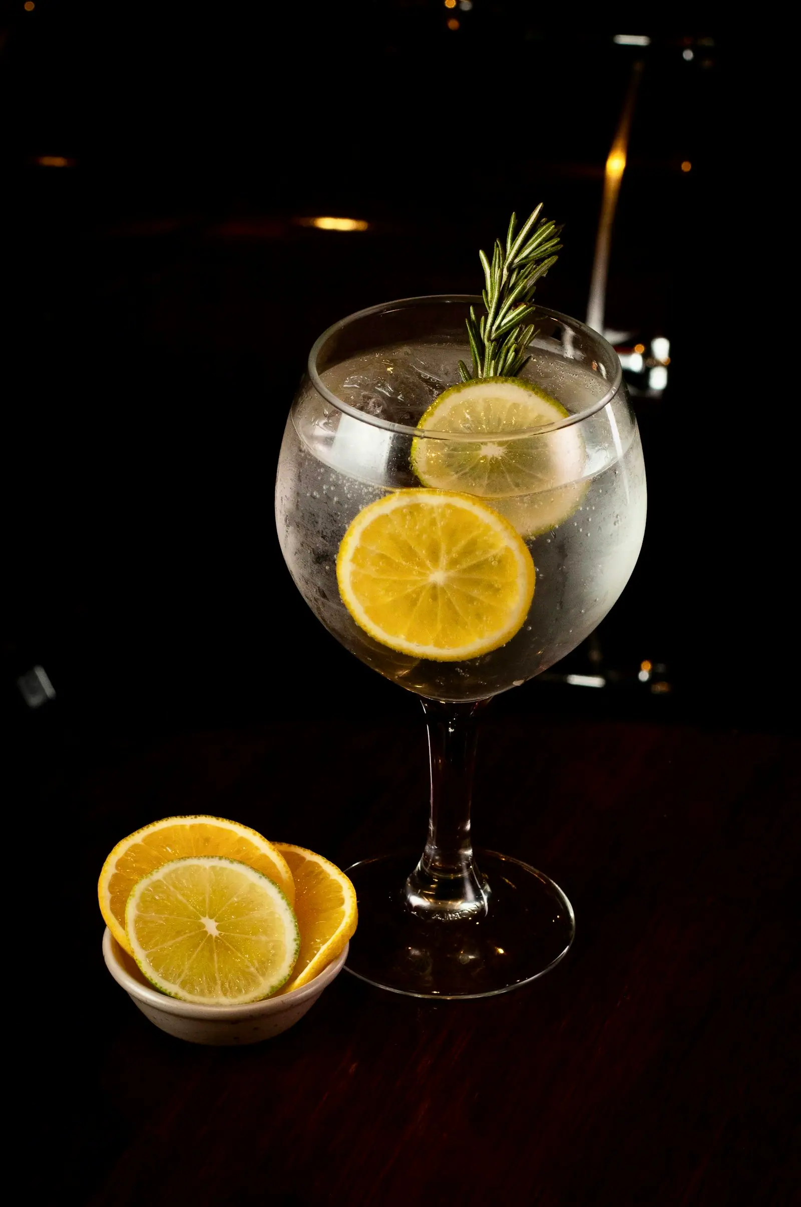 Copo balão com gin e tônica, rodelas de limão e um ramo de alecrim.
